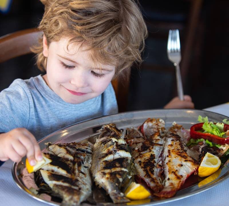 Niño comiendo pescado rico en omega-3 como protección contra la miopía.