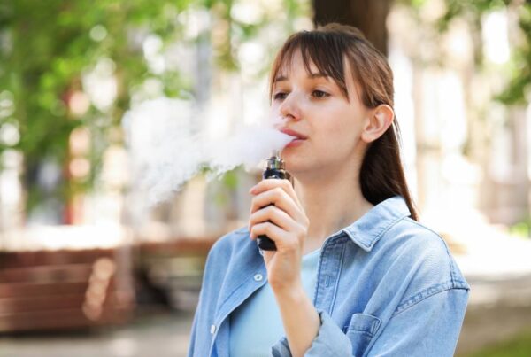 Joven vapeando al aire libre con un dispositivo electrónico.