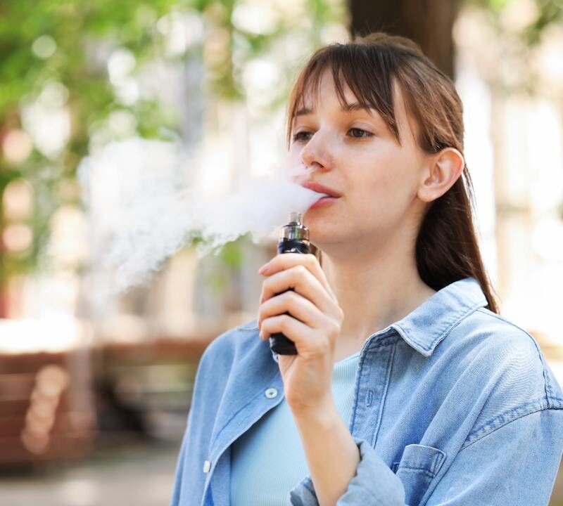 Joven vapeando al aire libre con un dispositivo electrónico.