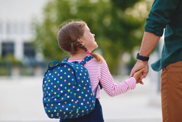 Niños entrando a la escuela con mochilas y padres acompañándolos