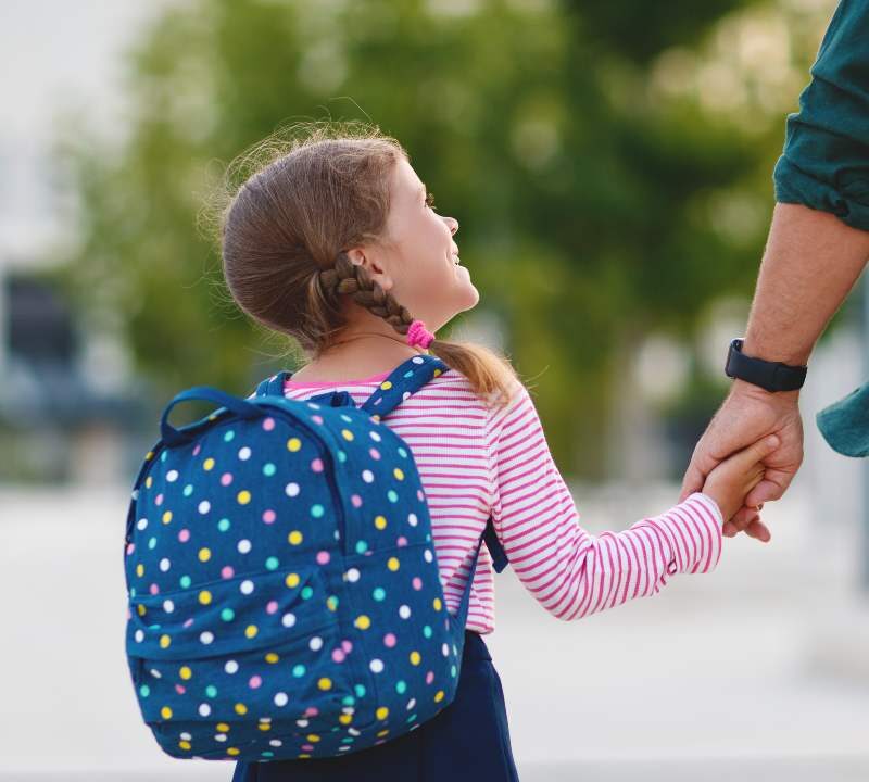 Niños entrando a la escuela con mochilas y padres acompañándolos