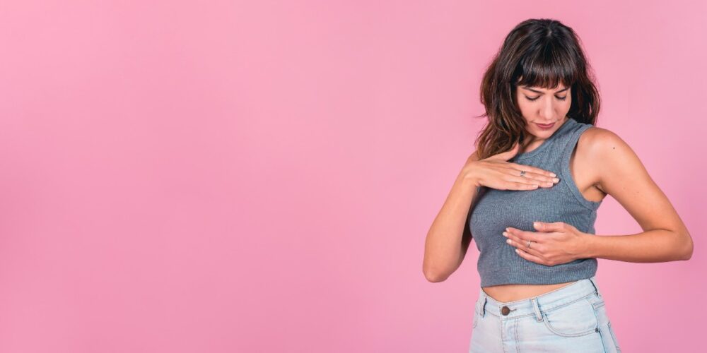 Mujer revisándose los senos con informe médico de cáncer de mama