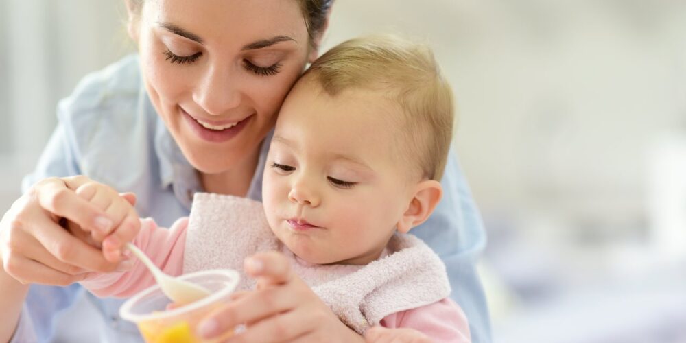 Madre alimentando a su bebé con frutas en casa mientras juegan 