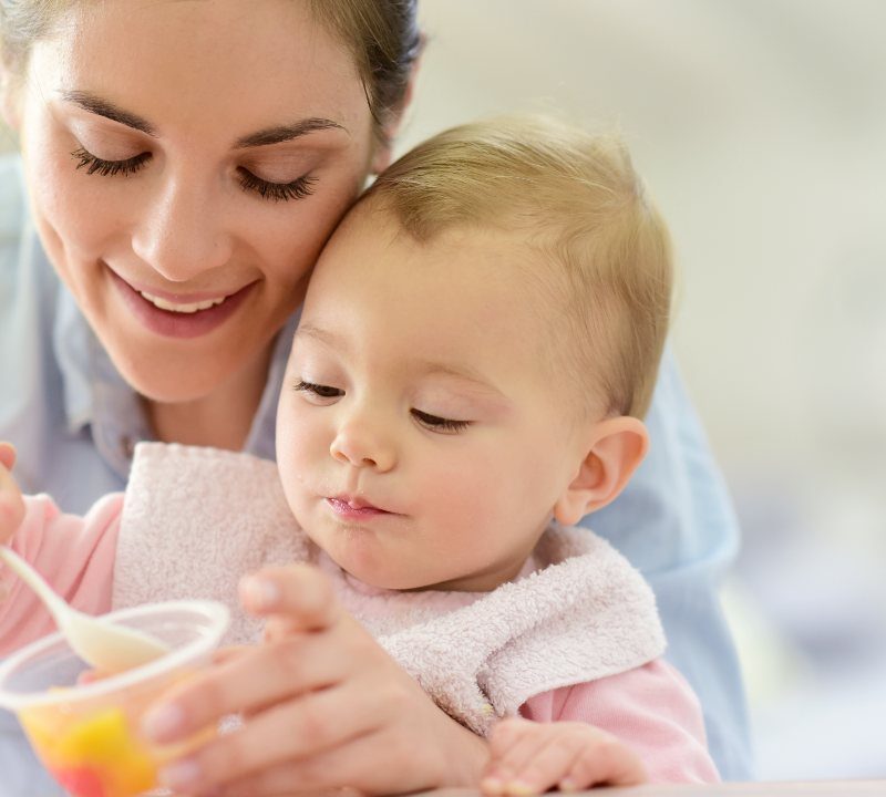 Madre alimentando a su bebé con frutas en casa mientras juegan 