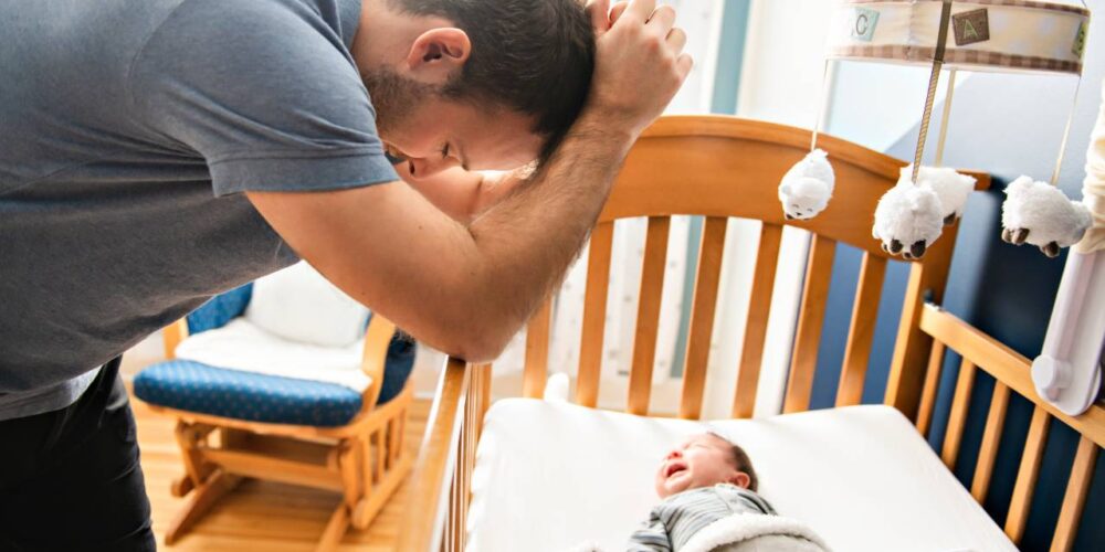 Padre con su bebé en brazos, con gesto de cansancio y reflexión.