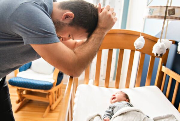 Padre con su bebé en brazos, con gesto de cansancio y reflexión.