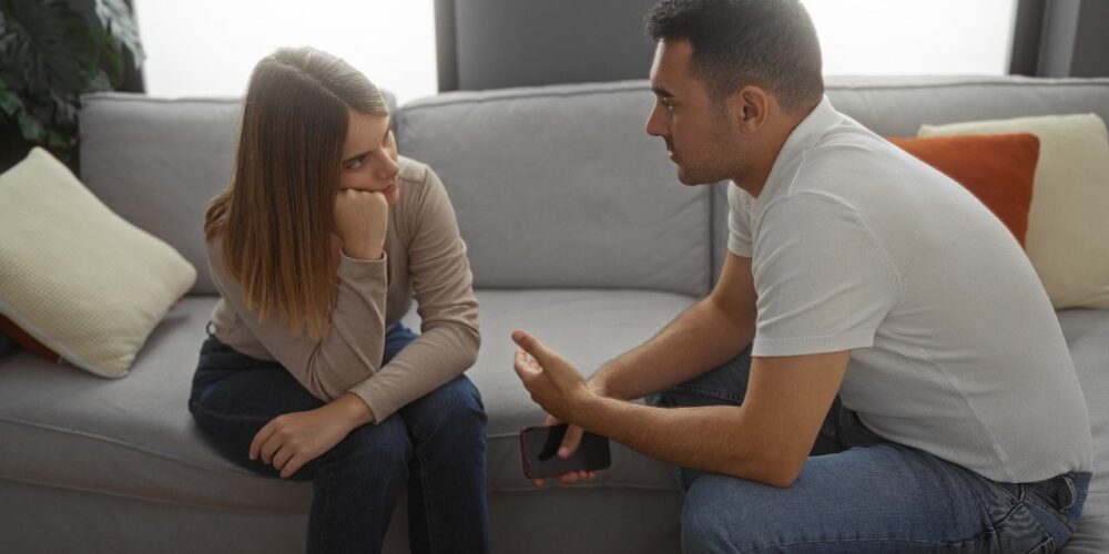 Pareja conversando seriamente en un sofá, mostrando una charla íntima y reflexiva.