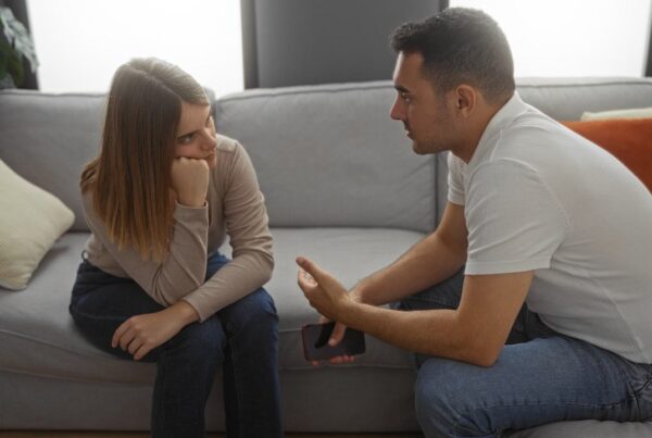 Pareja conversando seriamente en un sofá, mostrando una charla íntima y reflexiva.