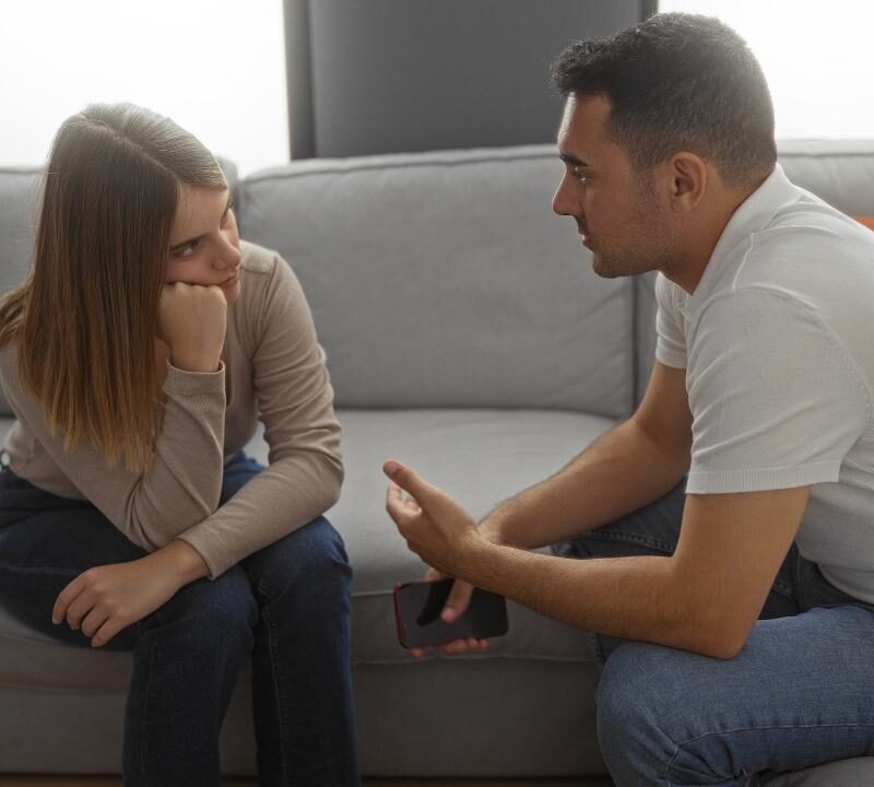 Pareja conversando seriamente en un sofá, mostrando una charla íntima y reflexiva.
