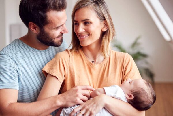 Pareja abrazándose mientras cuidan a su bebé en casa