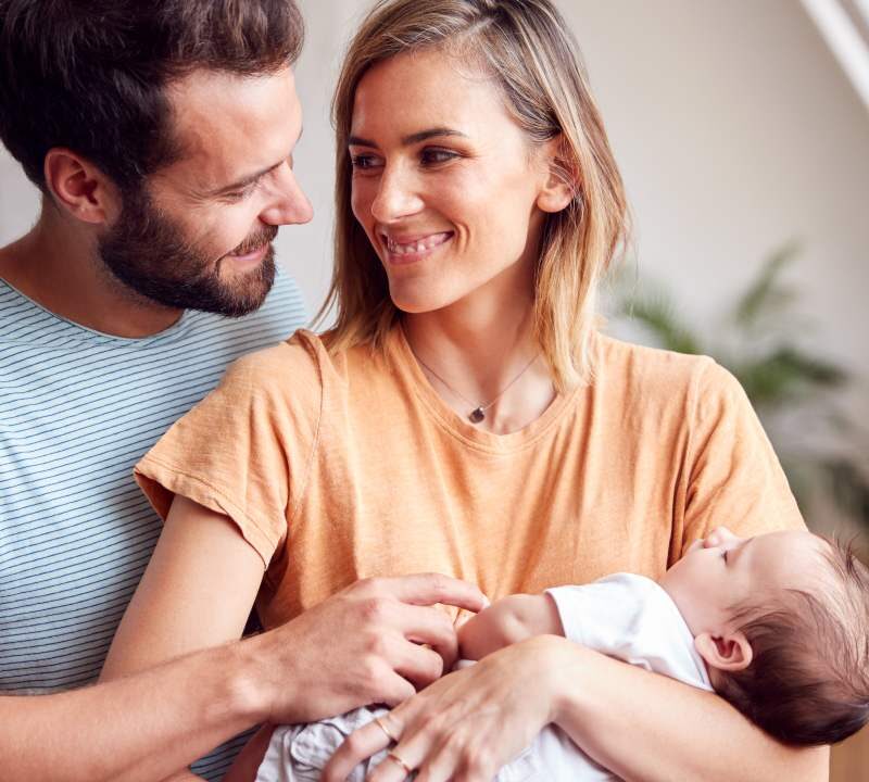 Pareja abrazándose mientras cuidan a su bebé en casa