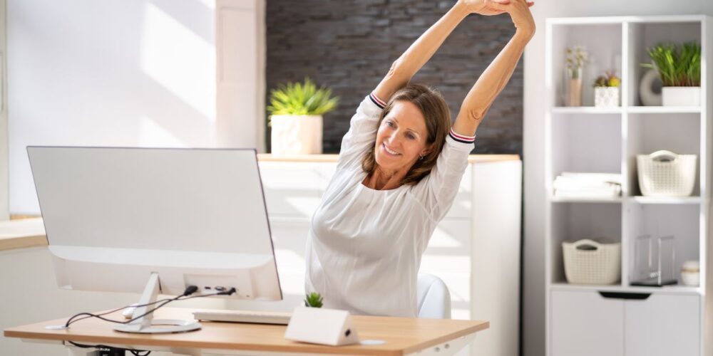 Mujer realizando estiramientos en su escritorio para contrarrestar el sedentarismo