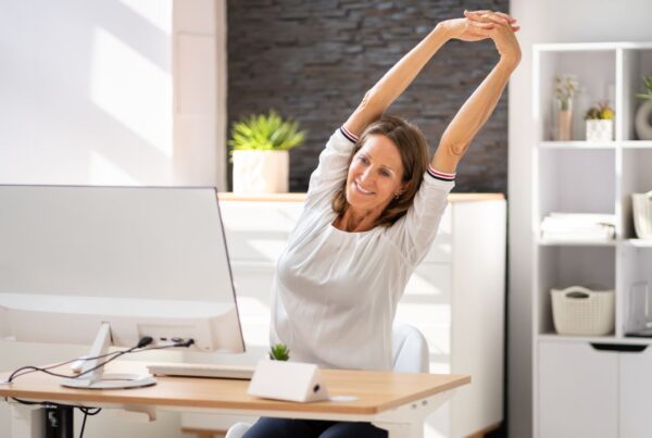 Mujer realizando estiramientos en su escritorio para contrarrestar el sedentarismo