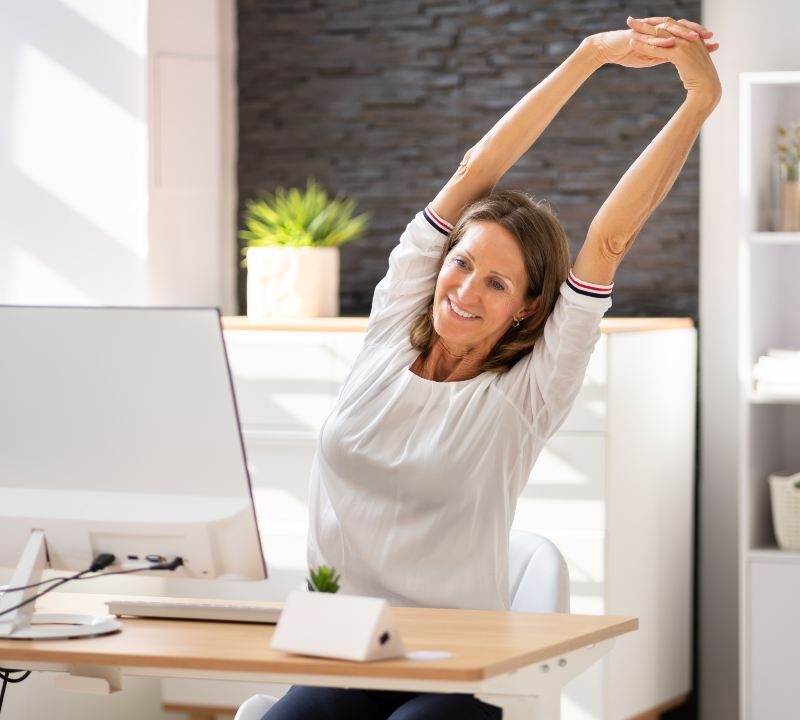 Mujer realizando estiramientos en su escritorio para contrarrestar el sedentarismo