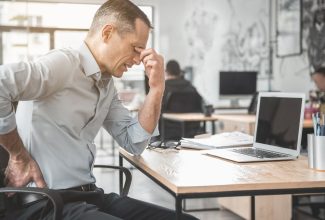 Empleado de oficina tocándose la espalda por dolor causado al pasar demasiadas horas sentado
