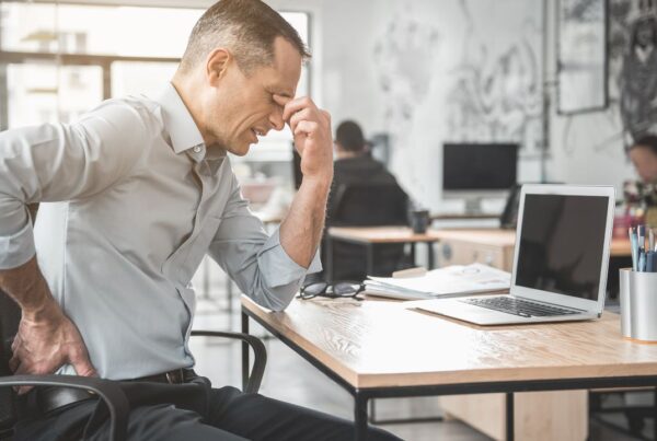 Empleado de oficina tocándose la espalda por dolor causado al pasar demasiadas horas sentado