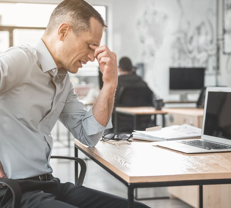 Empleado de oficina tocándose la espalda por dolor causado al pasar demasiadas horas sentado