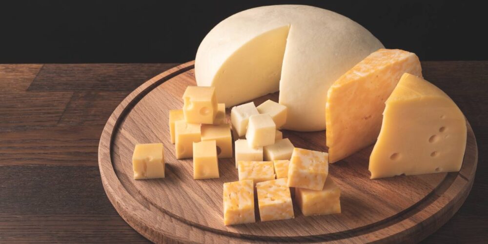 Variedad de quesos grasos como cheddar y brie sobre una tabla de madera.