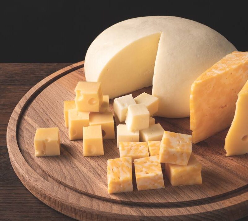 Variedad de quesos grasos como cheddar y brie sobre una tabla de madera.