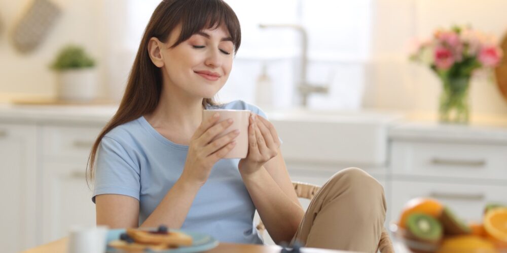 Persona sonriente sosteniendo una taza humeante, ilustrando los beneficios del consumo de café en la salud mental.