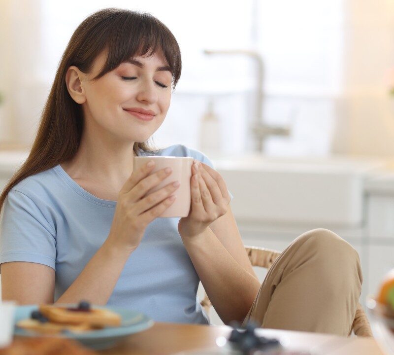 Persona sonriente sosteniendo una taza humeante, ilustrando los beneficios del consumo de café en la salud mental.