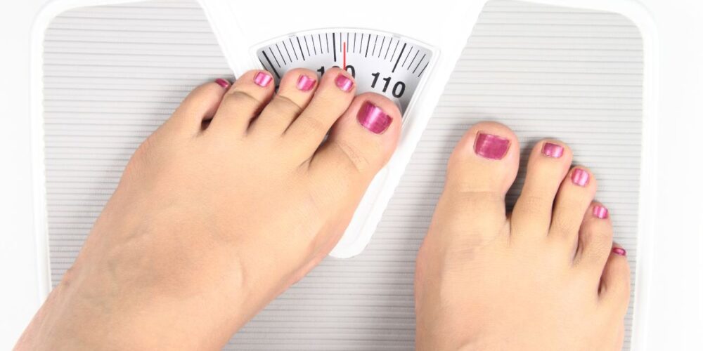 Persona de pie sobre una báscula observando el aumento de peso tras dejar el tratamiento.