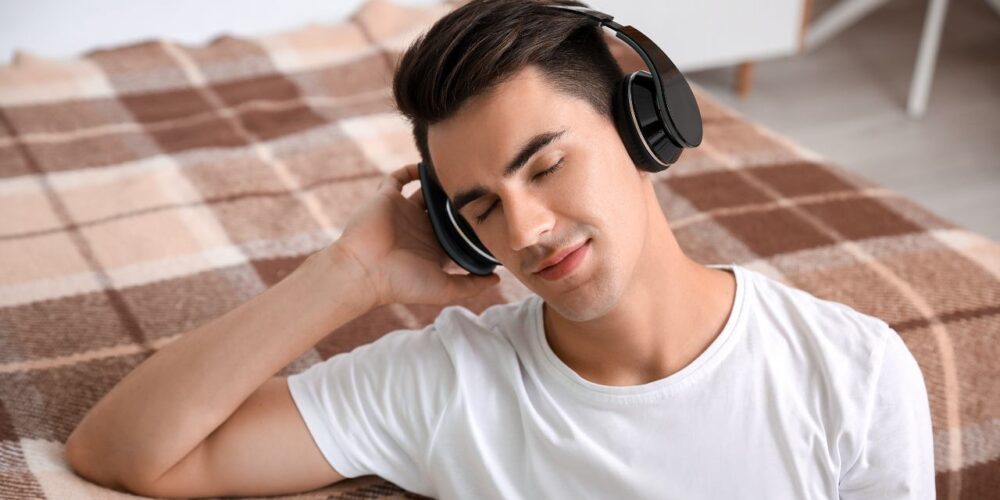 Persona joven escuchando música con auriculares con expresión reflexiva, ilustrando la relación entre estado de ánimo y música.
