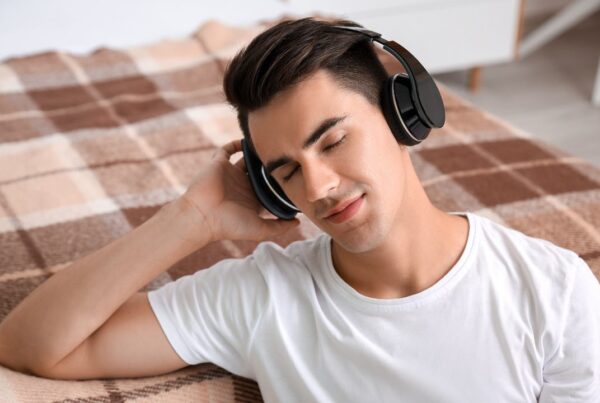 Persona joven escuchando música con auriculares con expresión reflexiva, ilustrando la relación entre estado de ánimo y música.