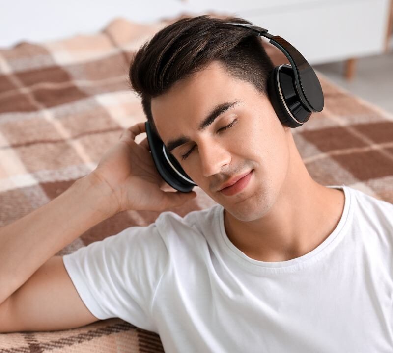 Persona joven escuchando música con auriculares con expresión reflexiva, ilustrando la relación entre estado de ánimo y música.