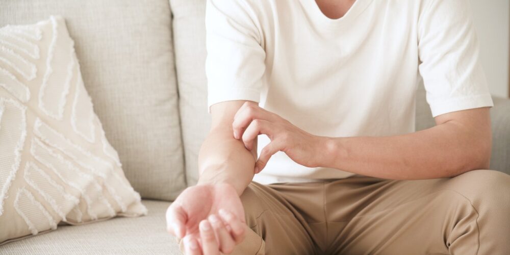 Persona rascándose el brazo por picor persistente sin lesiones visibles