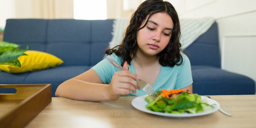 Mujer preocupada frente a un plato de comida, representando los efectos de las dietas muy bajas en calorías en el metabolismo y la salud mental