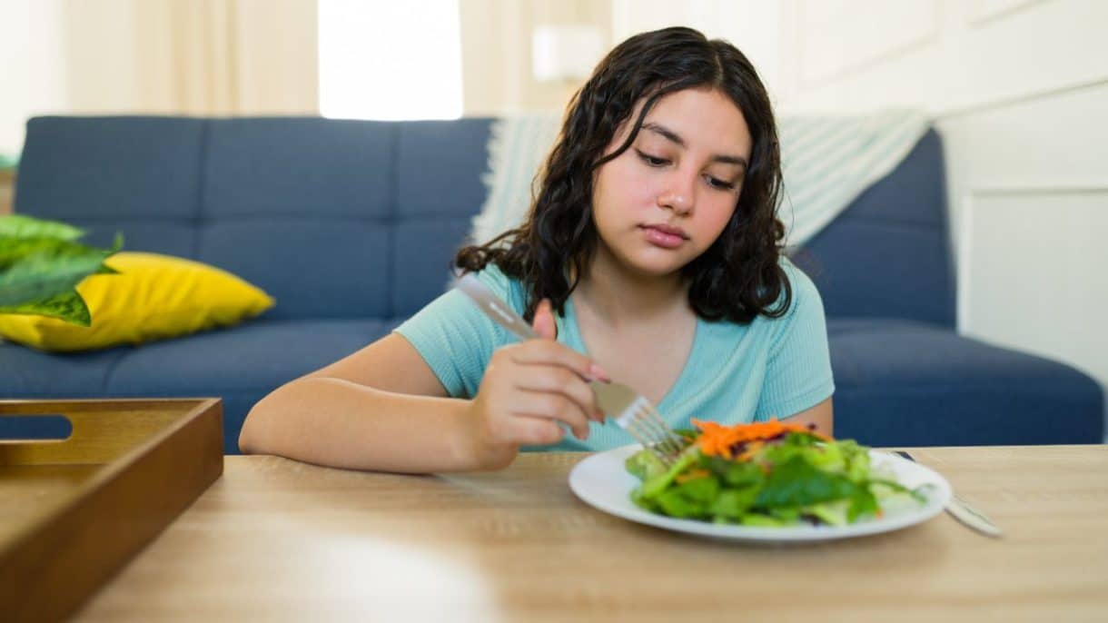 Mujer preocupada frente a un plato de comida, representando los efectos de las dietas muy bajas en calorías en el metabolismo y la salud mental