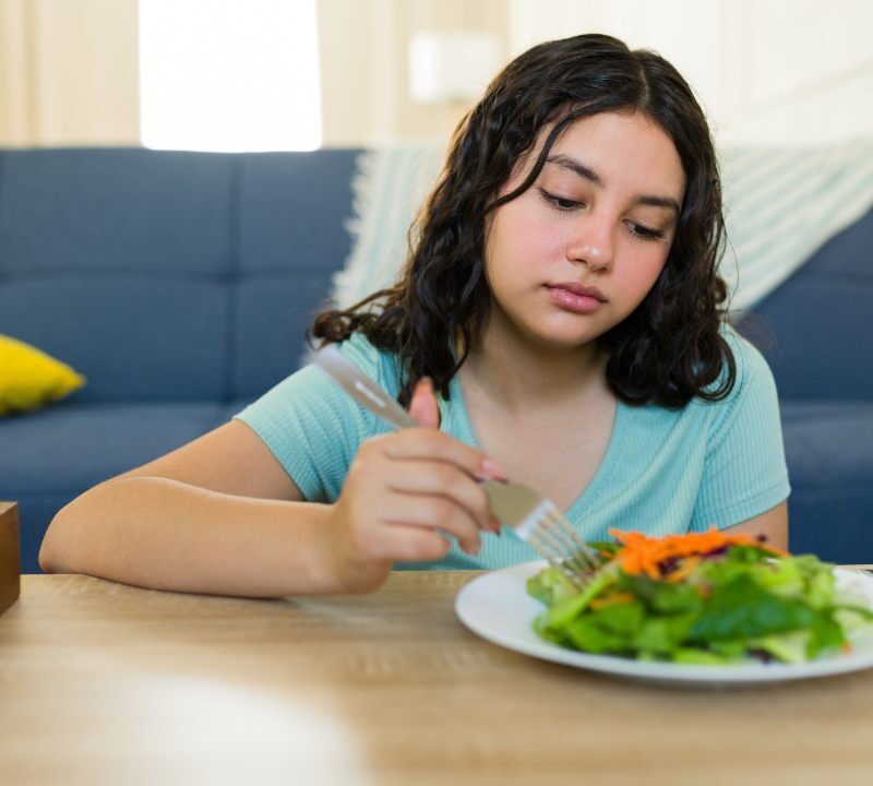 Mujer preocupada frente a un plato de comida, representando los efectos de las dietas muy bajas en calorías en el metabolismo y la salud mental