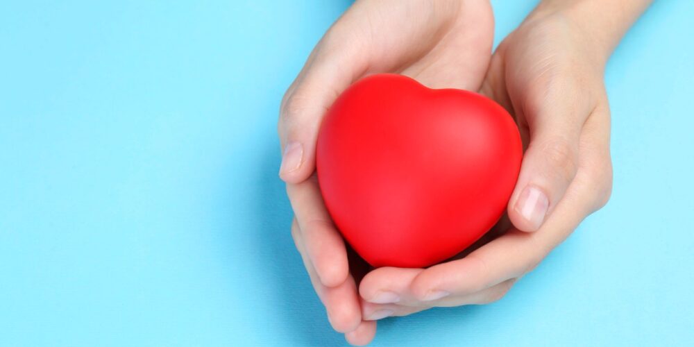 Representación visual de un corazón protegido por manos humanas sobre un fondo suave.