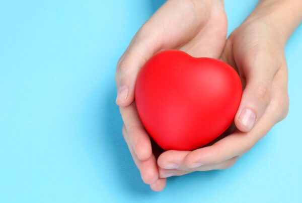 Representación visual de un corazón protegido por manos humanas sobre un fondo suave.