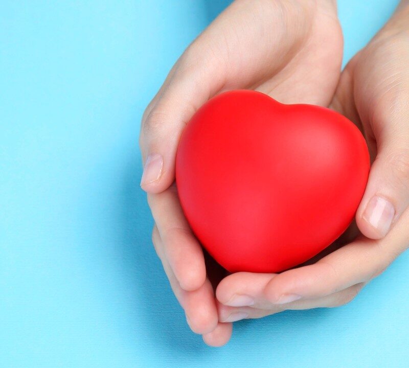 Representación visual de un corazón protegido por manos humanas sobre un fondo suave.