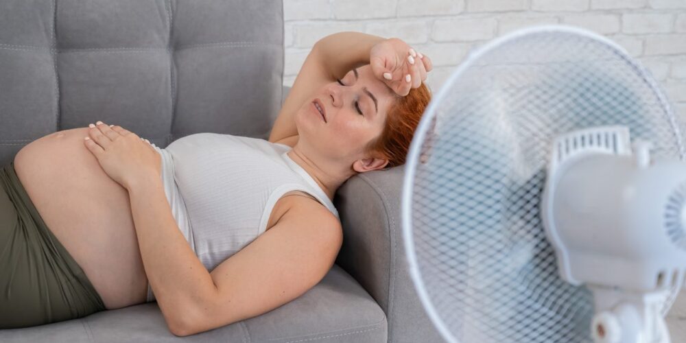 Mujer embarazada frente a ventilador en un ambiente caluroso para evitar efectos del calor