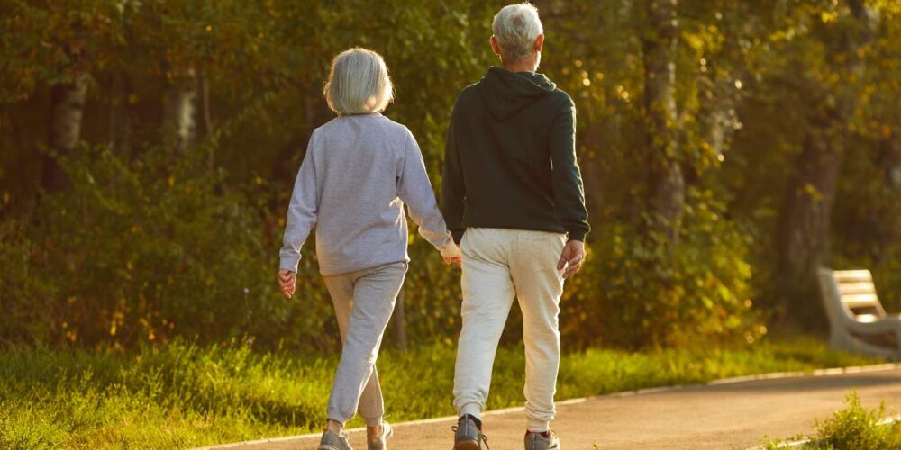 Una persona mayor caminando con paso firme por un sendero arbolado durante una mañana soleada, reflejando el beneficio del ejercicio para prevenir el Alzheimer.
