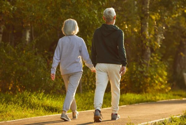 Una persona mayor caminando con paso firme por un sendero arbolado durante una mañana soleada, reflejando el beneficio del ejercicio para prevenir el Alzheimer.