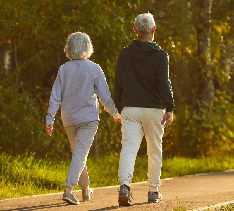 Una persona mayor caminando con paso firme por un sendero arbolado durante una mañana soleada, reflejando el beneficio del ejercicio para prevenir el Alzheimer.