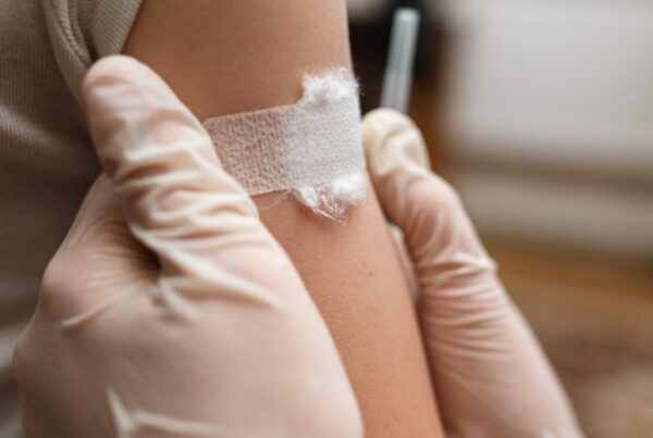 Primer plano de un pequeño parche circular sobre el hombro de un niño tras una inmunización, en un entorno clínico suave y luminoso que transmite seguridad y cuidado infantil.