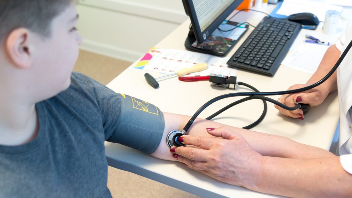 Un pediatra midiendo la presión arterial a un adolescente en una consulta médica, alertando sobre el aumento de la hipertensión pediátrica.