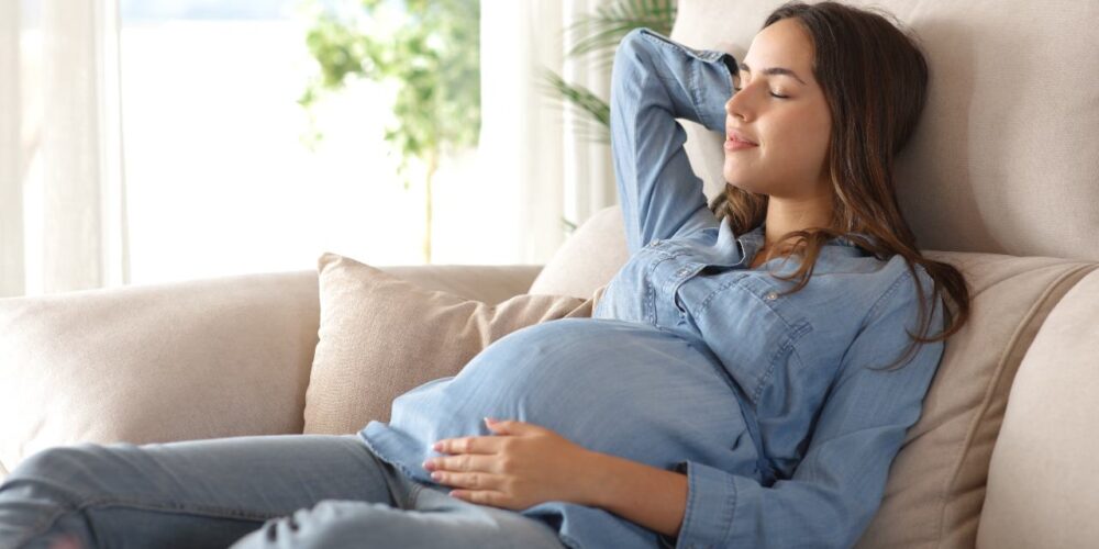 Mujer embarazada descansando en un interior fresco durante un día caluroso, representando la importancia de la protección térmica para la salud gestacional.