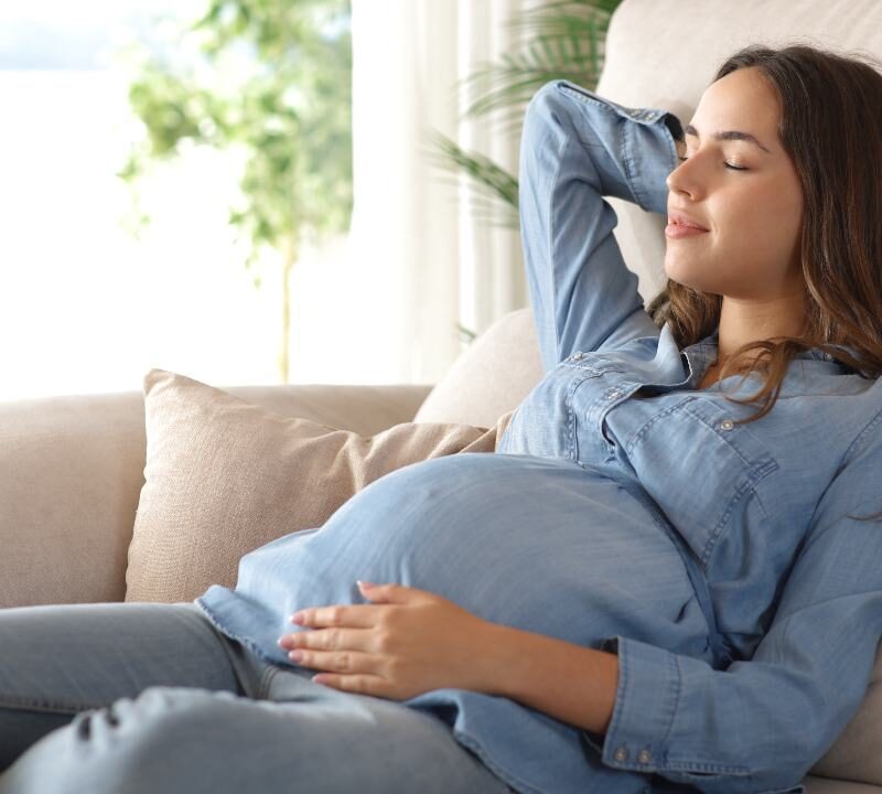 Mujer embarazada descansando en un interior fresco durante un día caluroso, representando la importancia de la protección térmica para la salud gestacional.