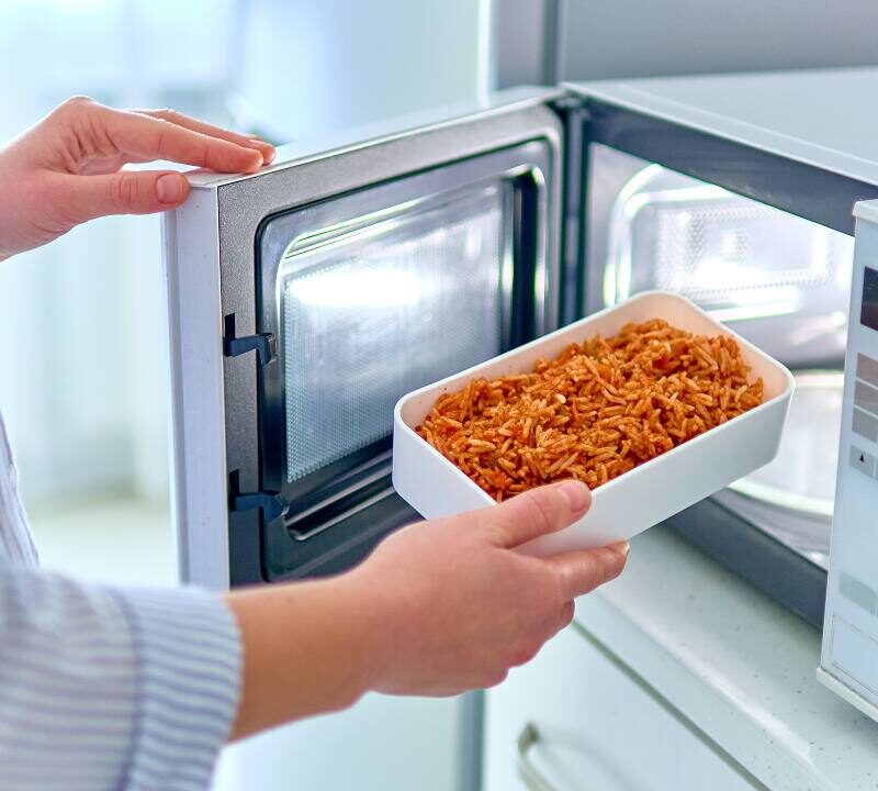 Persona utilizando microondas para calentar alimentos de forma segura