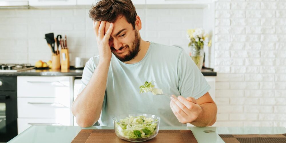 Persona cansada y pensativa frente a un plato pequeño de comida, que muestra cómo bajar calorías afecta el ánimo