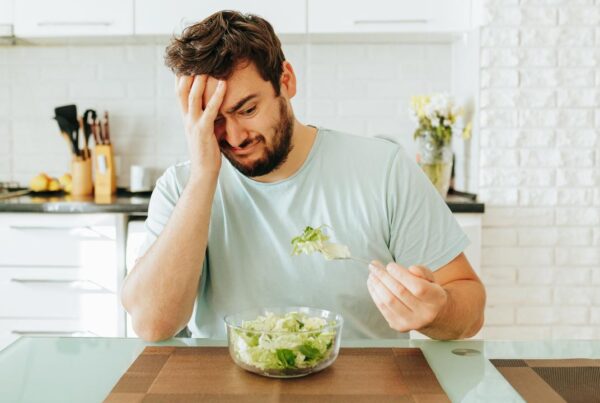 Persona cansada y pensativa frente a un plato pequeño de comida, que muestra cómo bajar calorías afecta el ánimo