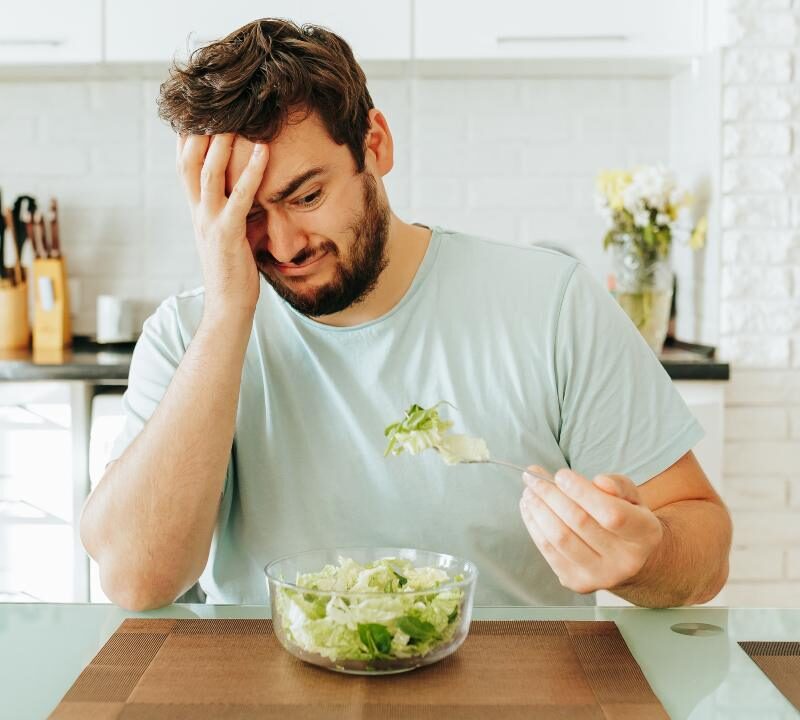 Persona cansada y pensativa frente a un plato pequeño de comida, que muestra cómo bajar calorías afecta el ánimo