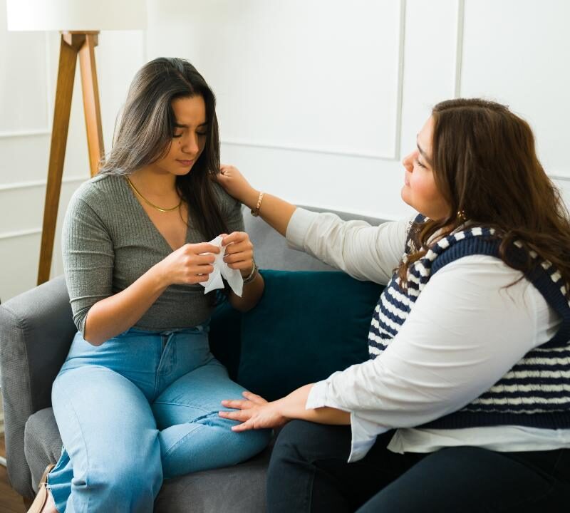 Mujer acompañando en silencio a una amiga triste mientras conversan en un sofá.